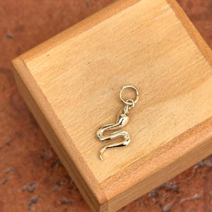 Könnte beinhalten: Ein goldener Schlangen-Anhänger mit einem Sprungring zum Anbringen an einer Halskette oder einem Armband.