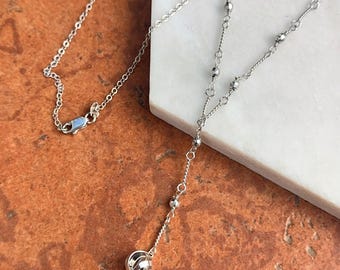 May include: A silver-toned necklace with a delicate chain and a dangling sphere pendant. The necklace features a Y-shaped design with small beaded accents and a lobster clasp closure. The pendant has a cage-like design.