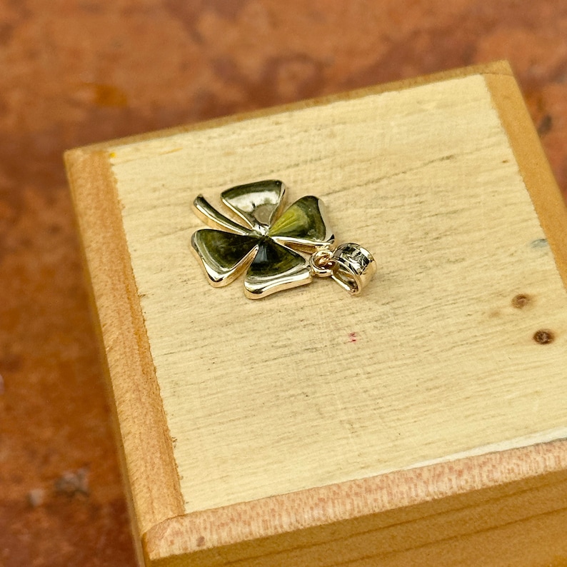 May include: A gold four-leaf clover charm pendant with a shiny finish. The pendant is on a wooden surface.