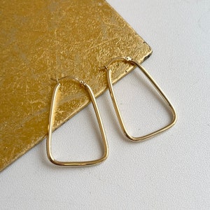 May include: A pair of gold triangle hoop earrings. The earrings are simple and elegant, and would make a great addition to any jewelry collection.