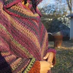 Puede incluir: Un chal de ganchillo multicolor con capucha. El chal est&aacute; hecho con hilo brillante y tiene un patr&oacute;n a rayas en tonos rosa, verde y morado.