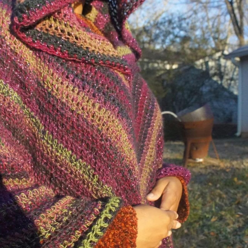 Puede incluir: Un chal de ganchillo multicolor con capucha. El chal est&aacute; hecho con hilo brillante y tiene un patr&oacute;n a rayas en tonos rosa, verde y morado.