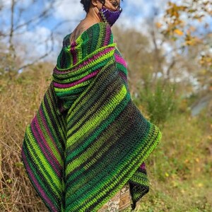 Puede incluir: Un chal con capucha de ganchillo a rayas verdes, negras y moradas con un borde de flecos.