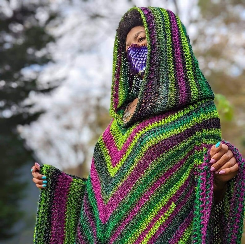 Puede incluir: Un poncho de ganchillo con capucha de color verde, morado y negro con un patr&oacute;n geom&eacute;trico. El poncho tiene una capucha grande y un dise&ntilde;o largo y fluido.