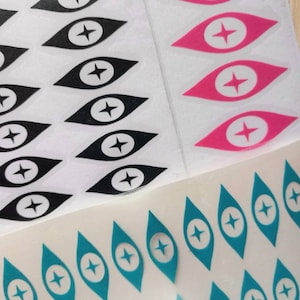 May include: Three sheets of stickers with a white background and a repeating pattern of black, pink, and teal eye-shaped designs with a white star in the center.