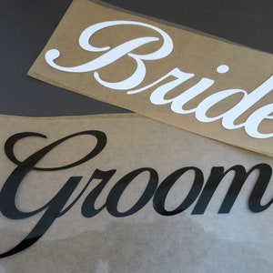 Könnte beinhalten: Zwei Blätter Papier mit den Wörtern "Bride" und "Groom" in Kursivschrift. Das Wort "Bride" ist weiß und das Wort "Groom" ist schwarz.