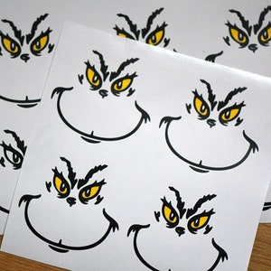 May include: Sheets of white stickers featuring a cartoon face with yellow eyes, a black frown, and a wide, curved smile. The stickers have a mischievous expression, and are likely themed for a holiday or character.