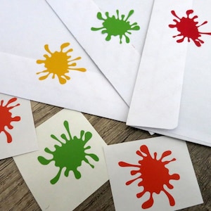 Peut inclure: Cinq éclaboussures de peinture colorées sur du papier blanc. Les éclaboussures sont rouges, vertes, jaunes et orange. Les éclaboussures sont sur des enveloppes et de petits carrés de papier.