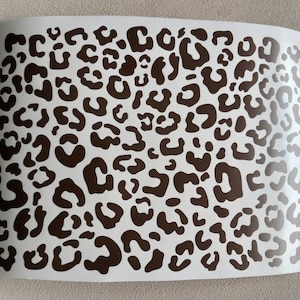 Könnte beinhalten: Ein weißer Hintergrund mit einem braunen Leopardenmuster. Der Druck besteht aus vielen Flecken unterschiedlicher Größe.