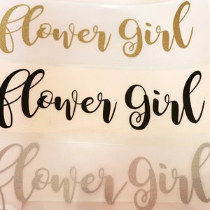 Könnte beinhalten: Drei Versionen des Satzes "Flower Girl" in verschiedenen Stilen. Die obere Version ist in Goldglitter, die mittlere Version ist schwarz und die untere Version ist in Silberglitter.