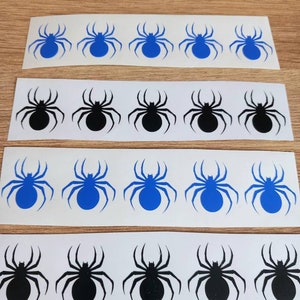 Op de afbeelding: Vier rijen spin stickers op witte vellen. De bovenste rij heeft vijf blauwe spinnen. De tweede rij heeft vijf zwarte spinnen. De derde rij heeft vijf blauwe spinnen. De onderste rij heeft vijf zwarte spinnen.