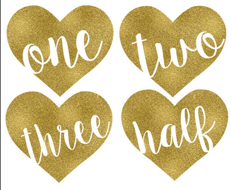 May include: Four gold glitter heart-shaped decorations with the words "one", "two", "three", and "half" written in white.