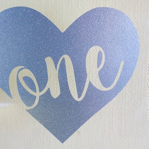 May include: A blue glitter heart with the word "one" in white script inside.