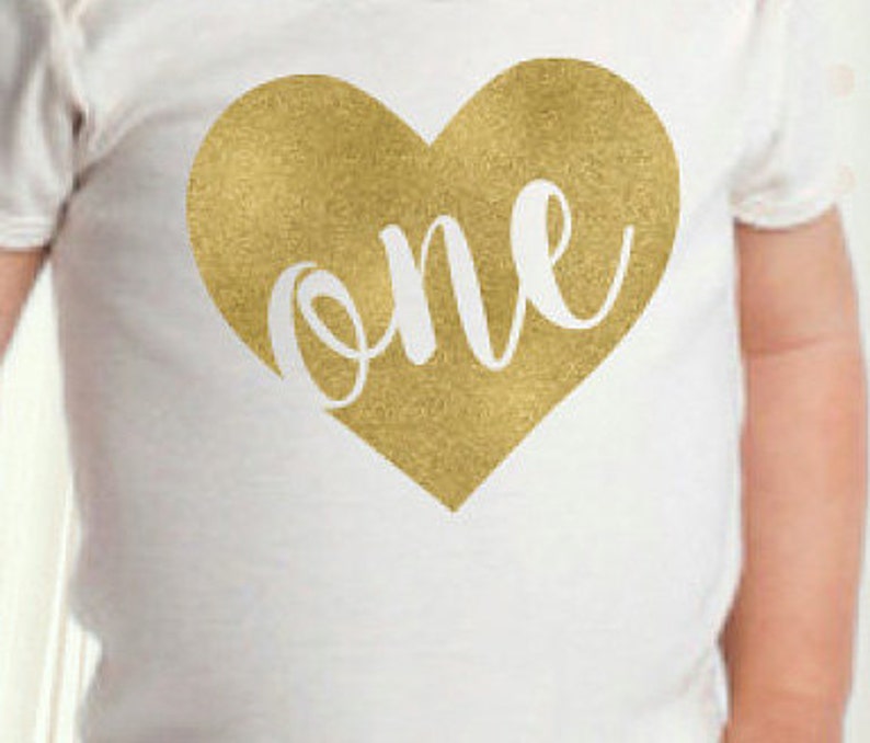 May include: White baby onesie with a gold glitter heart that says "one" in white cursive lettering.