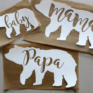 Pode incluir: Três recortes de silhueta de urso de vinil branco com as palavras "baby", "mamã" e "papá" escritas dentro de cada urso.
