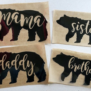 Op de afbeelding: Vier zwarte beren-silhouet vinyl stickers met de woorden "mama", "sister", "daddy" en "brother" in gouden letters.