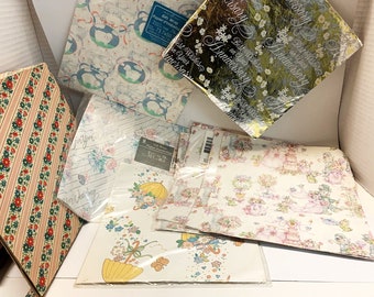 May include: Assortment of gift wrap paper in various patterns and colours.  The papers include a silver foil paper with the text "Best Wishes on Your Anniversary", a white paper with a floral pattern and the text "For Your Wedding", a white paper with a pink and green pattern featuring a wedding couple, a white paper with a blue and white pattern featuring sheep, and a white paper with a pink and green pattern featuring a yellow umbrella.