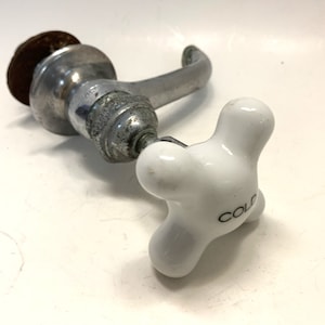 May include: A vintage chrome faucet with a white porcelain cold water handle. The handle has a four-point star shape and the word "COLD" is printed on it.