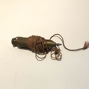 May include: A brass plumb bob with a brown string attached. The string is wrapped around the bob and is loose.