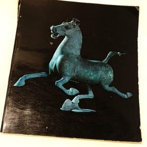 May include: A teal blue bronze sculpture of a horse in a running pose against a black background.