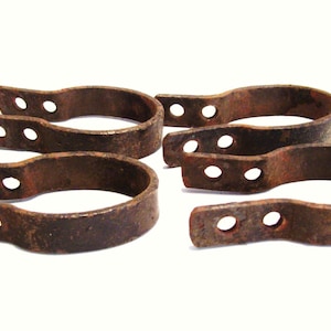 May include: Four rusty metal clamps with multiple holes. The clamps are in various positions and are all slightly different in size and shape.