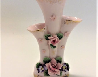 May include: A pink porcelain vase with three openings, decorated with pink and purple flowers and gold accents.