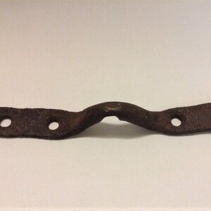 May include: A rusty metal strap with four holes and a curved section in the middle.