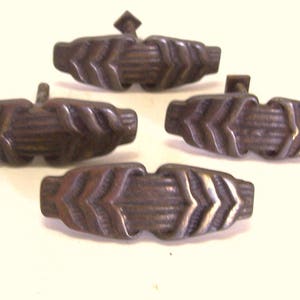 May include: Four antique metal drawer pulls with a chevron pattern. The pulls are a dark brown colour and have a slightly distressed finish.