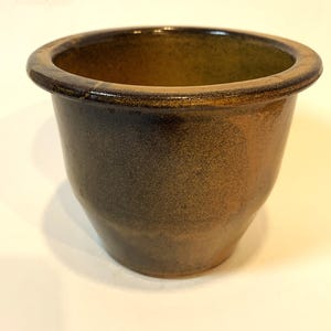 May include: A glazed ceramic pot with a wide, rounded rim. The pot has a speckled, earthy colour palette of brown, tan, and dark green. The interior is a darker shade of green. Suitable for plants or home decor. The pot is approximately 15 cm in diameter.