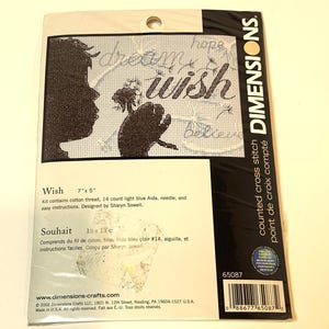 May include: A Dimensions counted cross stitch kit titled "Wish." The kit features a silhouette of a person blowing dandelion seeds, with the words "dream," "wish," "hope," and "believe." The kit measures 17.78 cm x 12.7 cm.
