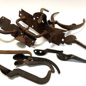 Peut inclure: Une collection de ferrures de porte en métal rouillé antique, comprenant une poignée de porte, un loquet de porte et plusieurs charnières de porte. La quincaillerie est dans divers états d'usure, certaines pièces montrant des signes de rouille et de corrosion.