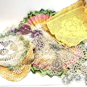 May include: A collection of crocheted doilies in various colours, including white, yellow, green, and purple. The doilies are made with delicate lace patterns and have a vintage aesthetic.