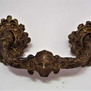 May include: Ornate brass door pull with a face in the centre and scrollwork on the sides.