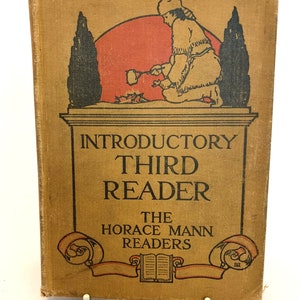 May include: A vintage book cover with a tan background and a black and white illustration of a person in a fur-trimmed hat and coat kneeling by a fire. The text on the cover reads "Introductory Third Reader The Horace Mann Readers".