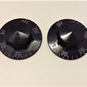 May include: Two black oven knobs with white markings. The knobs are labelled "OFF" and have numbers from 50 to 250.