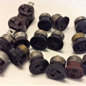 May include: A collection of 15 black and brown electrical outlet adapters. The adapters have a standard two-prong outlet and a light bulb socket.
