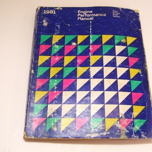 May include: A blue book with a geometric pattern of yellow, green, pink, and white triangles. The book is titled "Engine Performance Manual" and has the year "1981" printed on the cover.