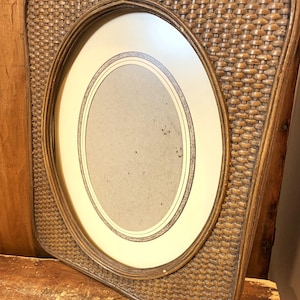 May include: A brown wicker picture frame with an oval opening and a white mount. The frame has a woven pattern.