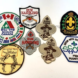 Peut inclure: Une collection de huit écussons brodés sur le thème du scoutisme. Les écussons sont de différentes couleurs et formes, dont un écusson rond avec le texte "Canadiens All" et un trèfle vert avec le texte "BCJ '77 Scouts Canada".