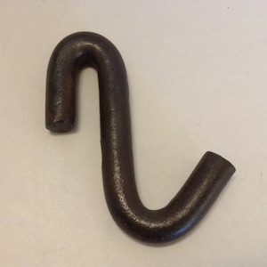 May include: A dark brown, curved metal hook with a textured surface. The hook has a rounded top and a shorter, angled bottom section. The object is likely used for hanging or securing items.