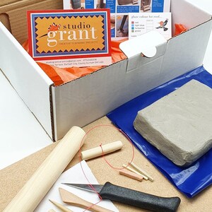 May include: A craft kit for making miniature houses. The kit includes clay, tools, and instructions. The box is white with a red and yellow logo that says "studio grant".
