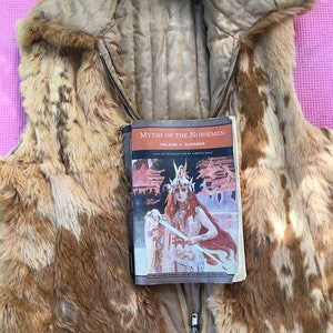 May include: A brown faux fur vest with a zip fastening and a button. A book titled "Myths of the Norsemen" by Helene A. Guerber is lying on top of the vest.