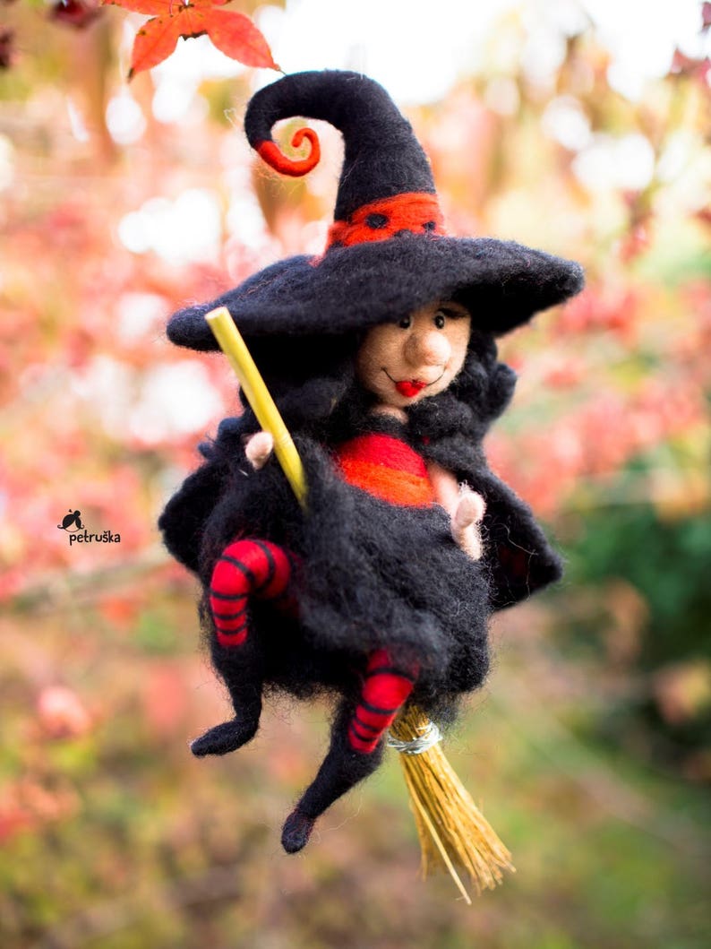 May include: A black felt witch doll with a red and black hat and a red and black striped dress, riding a brown broom.