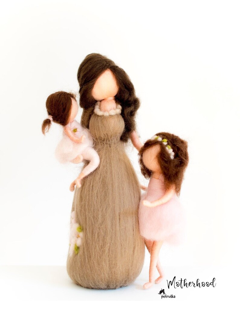 May include: A felt doll representing a mother with two daughters. The mother is wearing a brown dress and has long brown hair. The daughters are wearing pink dresses and have brown hair. The doll is handmade and has a whimsical, handcrafted look.