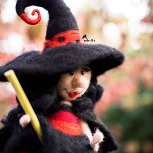 May include: A felt witch doll with a black hat, red and black dress, and a yellow broom. The doll has a friendly face with red lips and a black nose.