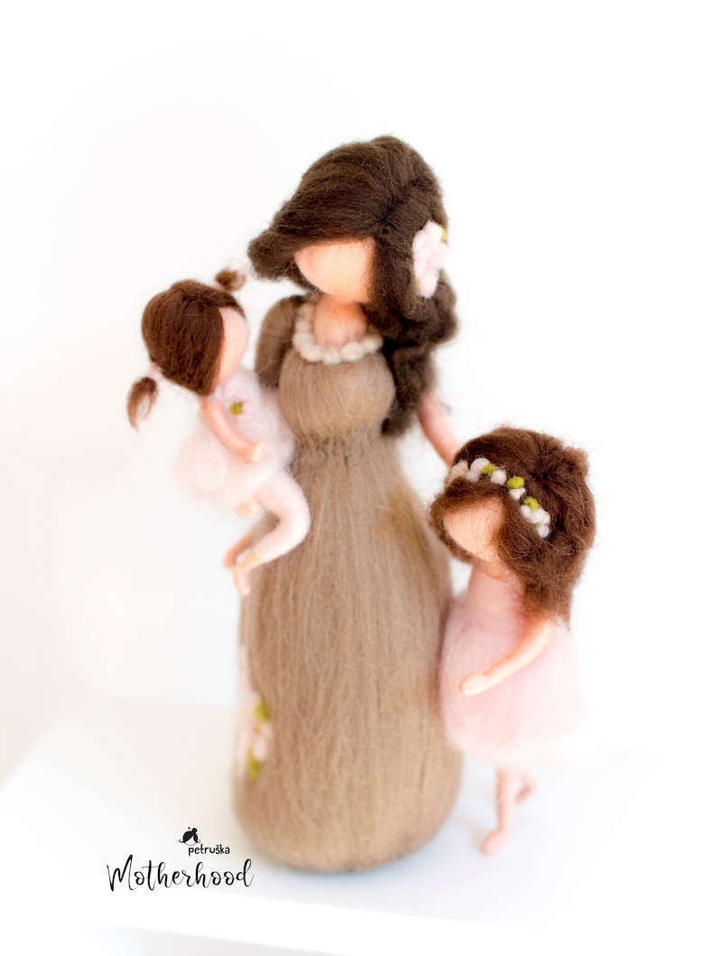 May include: A felt doll of a mother holding a smaller felt doll in her arms. A second smaller felt doll stands next to the mother. All three dolls have brown hair and are wearing pink dresses. The mother doll has a flower in her hair. The text "Petruska Motherhood" is at the bottom of the image.