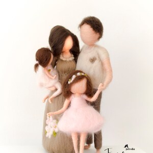 May include: A felt family figurine set with a mother, father, and two daughters. The mother is wearing a brown dress with white flowers, the father is wearing a beige shirt, and the daughters are wearing pink dresses. The family is standing together, holding hands.