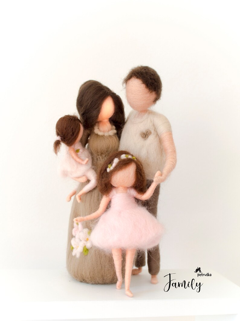 May include: A felt family figurine set with a mother, father, and two daughters. The mother is wearing a brown dress with white flowers, the father is wearing a beige shirt, and the daughters are wearing pink dresses. The family is standing together, holding hands.
