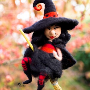 May include: A felt witch doll with a black hat, red and black striped stockings, and a long black dress is riding a straw broom.
