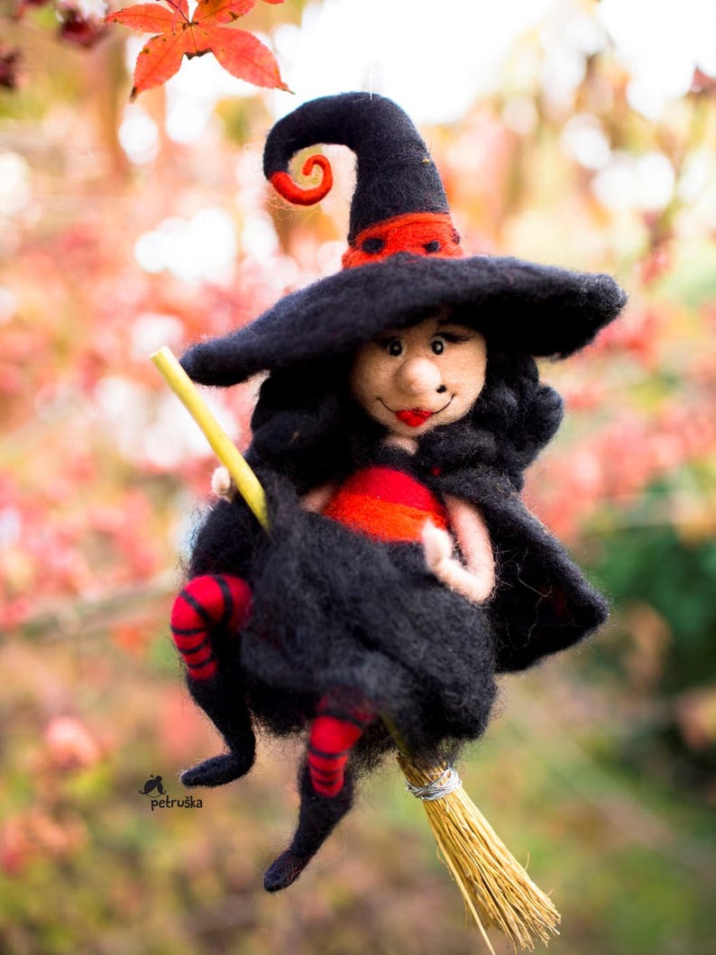 May include: A felt witch doll with a black hat, red and black striped stockings, and a long black dress is riding a straw broom.